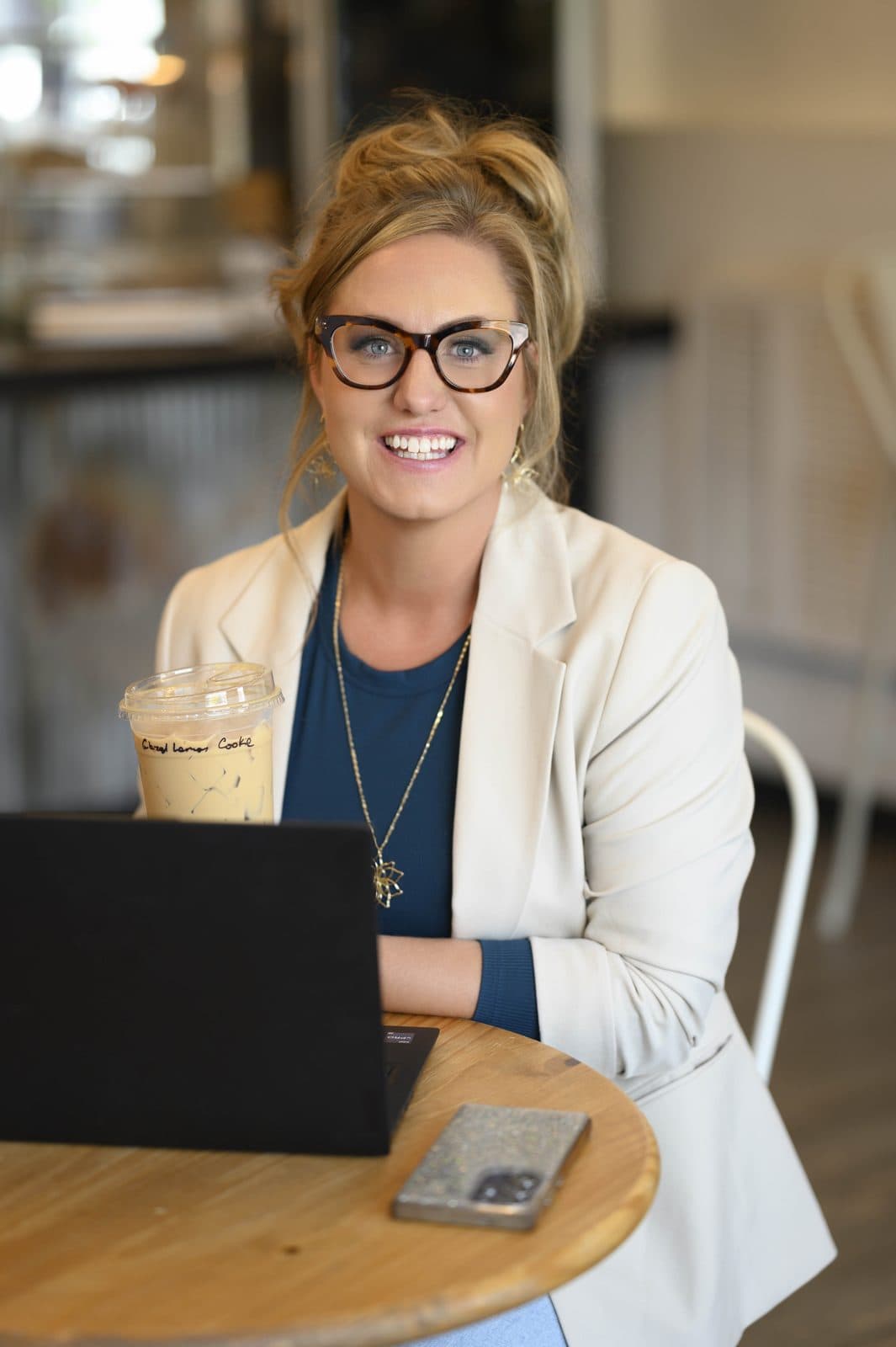 Jen smiling at her laptop in a cafe, iced coffee in hand